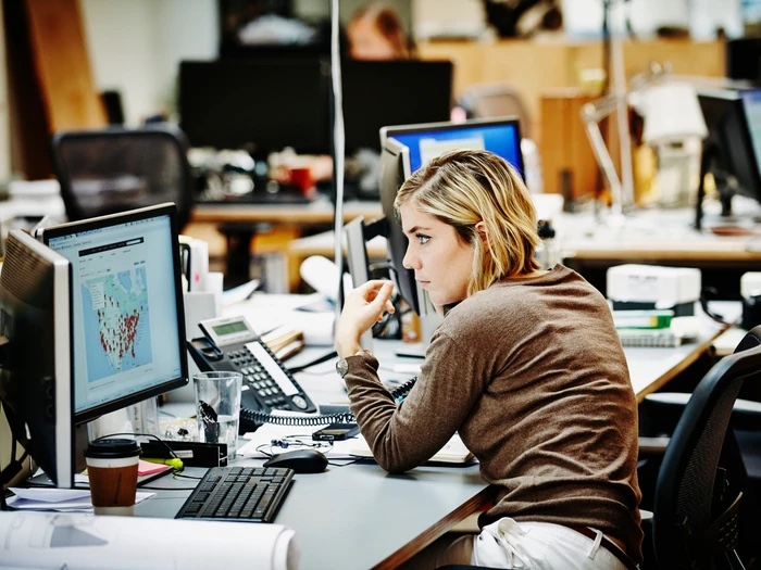 A woman at an office desk, reviewing data on her monitor